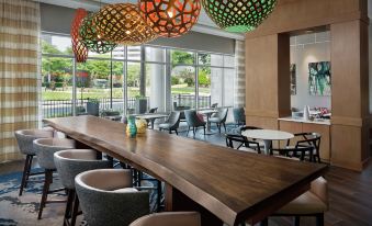 a large wooden dining table surrounded by chairs , with multiple pendant lights hanging from the ceiling at Hampton Inn & Suites Teaneck Glenpointe