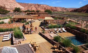 a group of people are gathered around a pool , some sitting on chairs and others standing near a pool , while others stand in the background at Nayara Alto Atacama