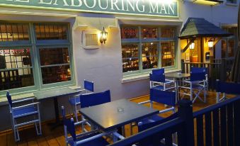 "a restaurant with a sign that says "" labouring man "" and blue chairs and tables outside" at The Labouring Man