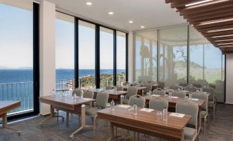 a conference room with tables and chairs , large windows , and a view of the ocean at Le Méridien Bodrum Beach Resort