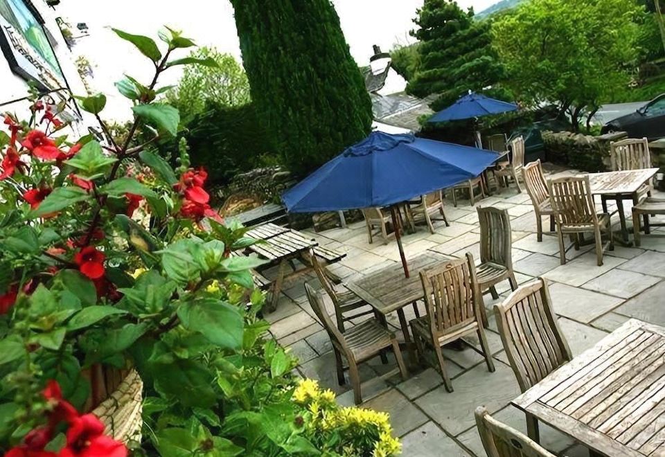 an outdoor dining area with wooden tables and chairs , surrounded by lush greenery and red flowers at Hare and Hounds