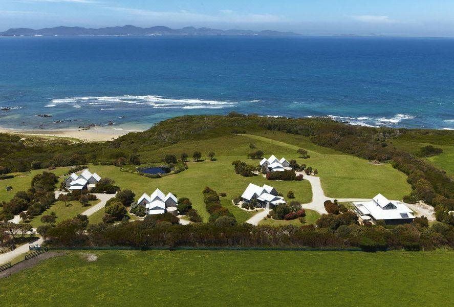 a large house surrounded by green grass and trees , with a beach in the background at Bear Gully Coastal Cottages