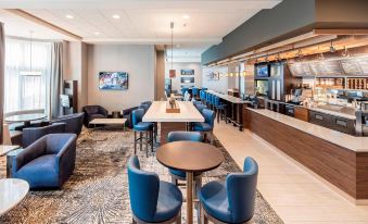 a modern hotel lobby with blue chairs , a bar area , and a dining table , all decorated in a well - decorated manner at Courtyard Boston Brookline