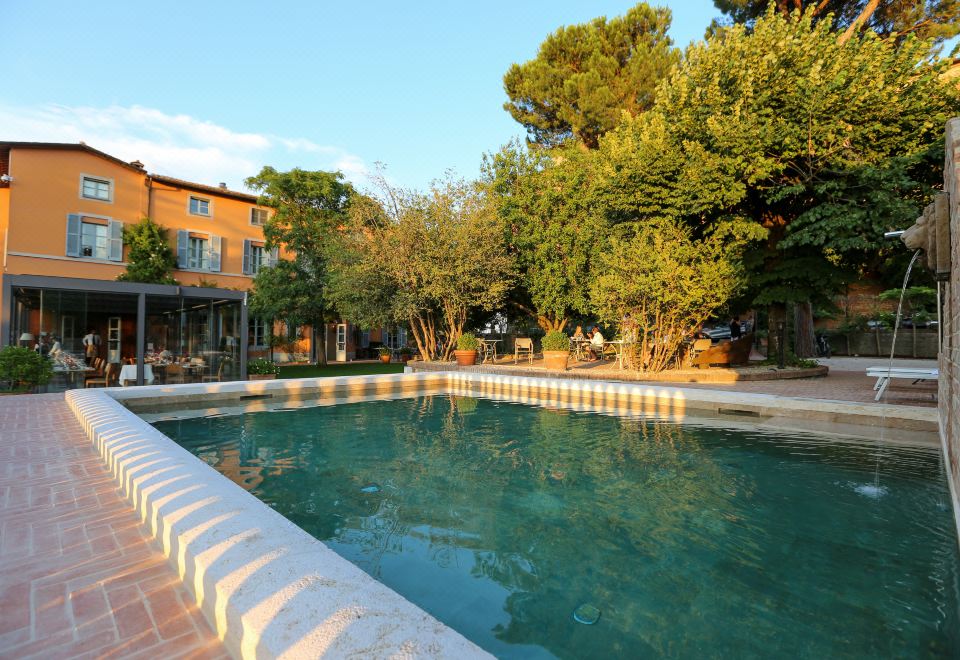 a large swimming pool is surrounded by a brick wall and trees , with a building in the background at Hotel Vannucci