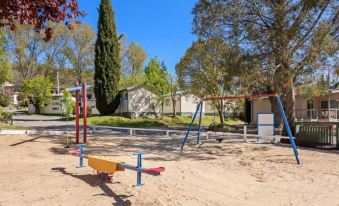 a sandy playground with various play equipment , including swings and slides , in a sunny setting at Discovery Parks - Jindabyne