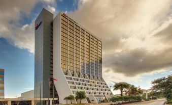 a large , modern hotel building with a unique , curved design under a cloudy sky in front of palm trees at Mobile Marriott