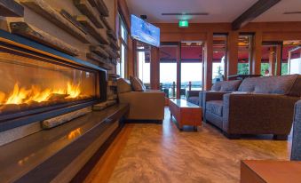 a cozy living room with wooden floors , large windows , and a fireplace , as well as comfortable furniture such as couches and chairs at Sproat Lake Landing Resort