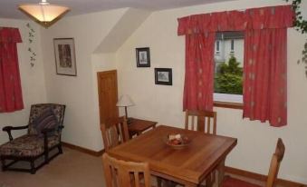 a dining room with a wooden table and chairs , red curtains , and framed pictures on the wall at Ardwell Bed & Breakfast