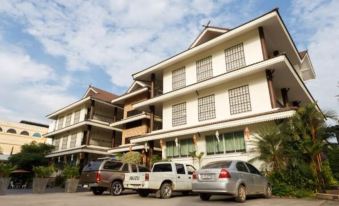 a row of cars parked in front of a large , two - story building with balconies and windows at Diamond Park Inn Chiangrai & Resort