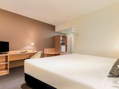 a large bed with a white comforter is in a room with a desk and chair at Ibis Melbourne Hotel and Apartments