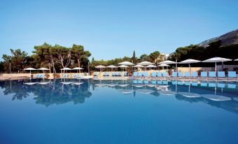 a large outdoor swimming pool surrounded by umbrellas , chairs , and trees , providing a relaxing atmosphere at Bluesun Hotel Elaphusa