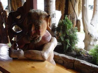 a wooden sculpture of a demon sitting on a table , with a plant in front of it at Troll