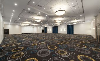 a large , empty conference room with a carpeted floor and multiple pendant lights hanging from the ceiling at Mercure Telford Centre Hotel
