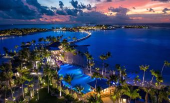 a beautiful tropical resort at sunset , with palm trees lining the water and a city skyline in the background at Hard Rock Hotel Maldives