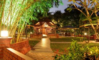 a wooden house surrounded by trees and a brick pathway leading up to the entrance at Aalankrita Resort and Convention