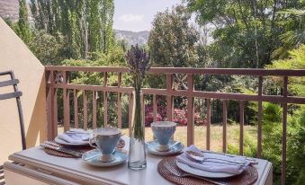 a table set with cups , plates , and utensils on a balcony overlooking a garden at Upper House Guesthouse