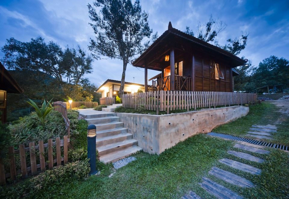 a wooden house with a thatched roof is surrounded by greenery and lit up at night at Bilut Hills @ Bentong
