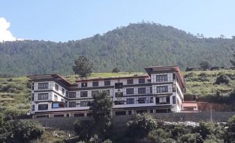 a large white building is situated on a hill overlooking a body of water , with mountains in the background at Hotel River Valley