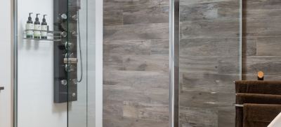 a shower door with a chrome finish is shown next to a wall with wooden tiles at The Swan Valley Retreat