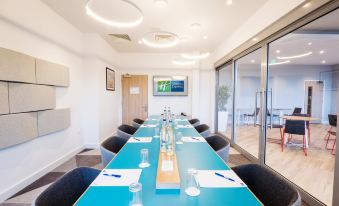 a long blue table with glasses and papers in the middle of a room with glass doors at Holiday Inn Express Stockport