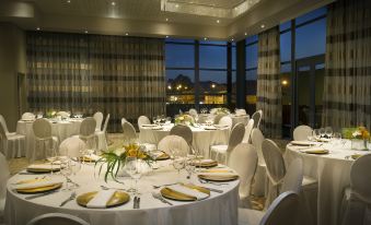 a well - decorated dining room with white tablecloths , gold accents , and a view of the city through large windows at Hilton Windhoek