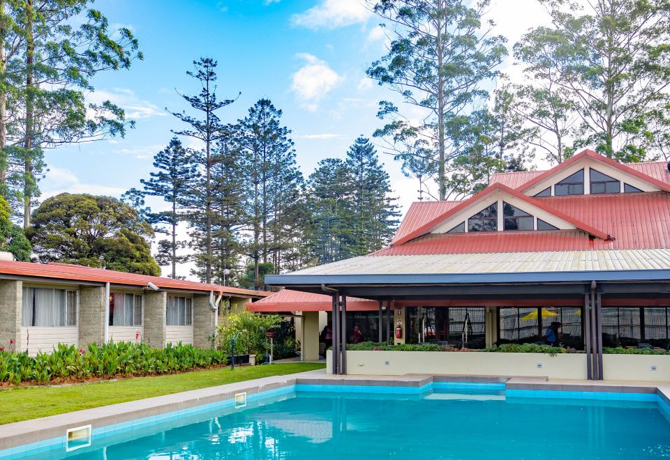 a large pool is surrounded by trees and a house with a red roof , surrounded by a body of water at Highlander Hotel