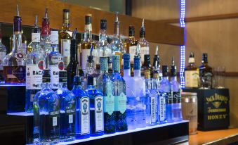 a bar with various bottles of alcohol on display , including some blue and white , in a dimly lit setting at Holiday Inn Express Stevenage