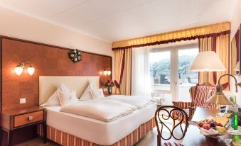 a large bed with white linens is in a room with a window and a desk at Bellevue Rheinhotel