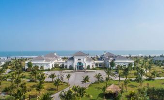 a large white building with a courtyard and palm trees in front of it , overlooking the ocean at Melia Vinpearl Cua Sot Beach Resort