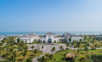 a large white house surrounded by palm trees and a beach , with the ocean in the background at Melia Vinpearl Cua Sot Beach Resort