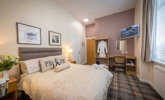 a clean and well - organized hotel room with a comfortable bed , a desk , and a tv at Castletown Hotel