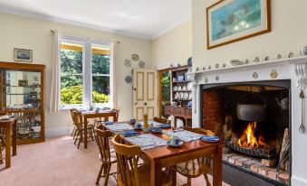 a dining room with a wooden table and chairs , a fireplace , and large windows at Cambridge House Breakfast & Bed
