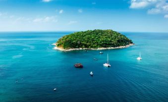 an aerial view of a small island surrounded by clear blue water , with several boats floating nearby at Beyond Patong