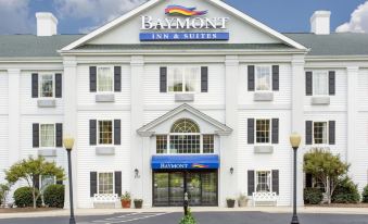 the baymont inn & suites hotel , a large white building with black shutters and blue awnings , stands in front of trees and a street at Comfort Inn