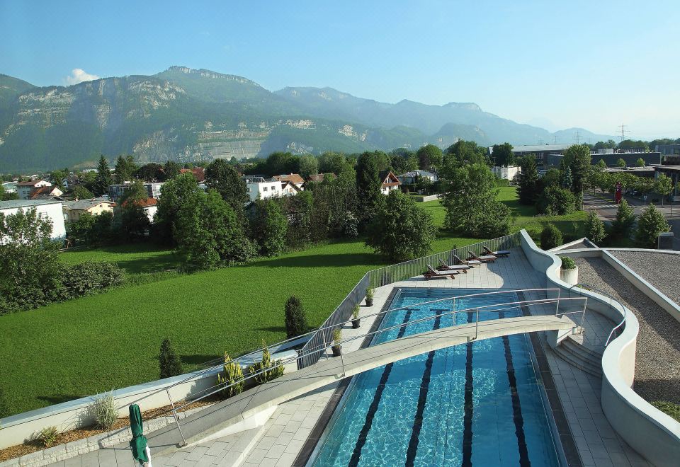 a large swimming pool with a mountain view in the background and trees surrounding the area at Four Points by Sheraton Panoramahaus Dornbirn