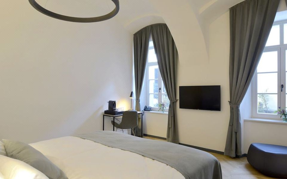 a modern bedroom with a white bed , grey curtains , and a flat - screen tv mounted on the wall at Hotel Maribor & Garden Rooms