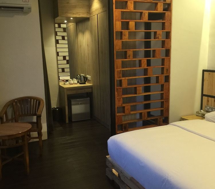 a modern bedroom with wooden walls , a bed , and a chair , along with a kitchenette in the background at The Oikos Hotel