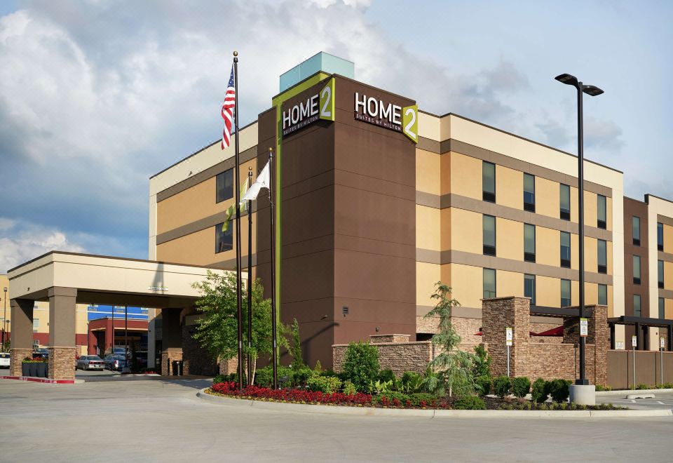 "a large hotel with a brown facade and the words "" home 2 "" on top is surrounded by flags" at Home 2 Suites by Hilton Muskogee