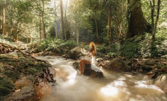 A woman sits on the rocks in front, surrounded by water, with trees behind her at La Lanna Resort