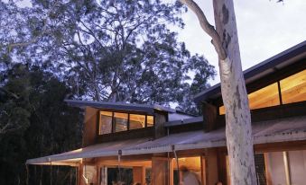 a restaurant with an open - air dining area and a large tree in the background during sunset at Paperbark Camp