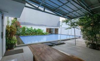 a modern house with a swimming pool , surrounded by greenery and a patio area with a table and chairs at Losmen Kebun Indah