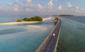 a man is walking on a wooden bridge over the ocean , surrounded by sandy islands at The Residence Maldives at Dhigurah