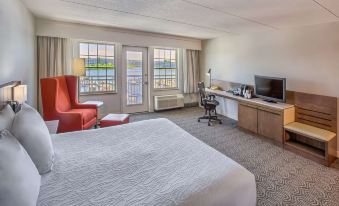 a modern hotel room with a white bed , red chair , and large window overlooking the ocean at Hilton Garden Inn Kent Island