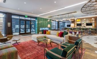 a modern living room with a white couch , red chair , and glass coffee table in front of large windows at Cambria Hotel - Arundel Mills BWI Airport