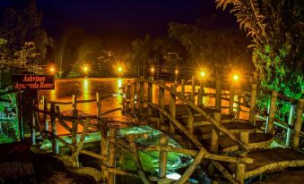 a wooden bridge over a body of water at night , illuminated by street lights and surrounded by trees at Rainforest Lodge, Deniyaya