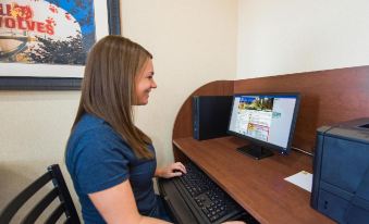 a woman in a blue shirt is sitting at a desk with a computer monitor and keyboard at My Place Hotel-Shakopee, MN