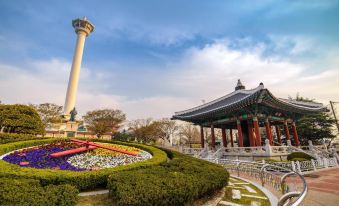 a traditional chinese pavilion surrounded by greenery , with a tall tower in the background and a colorful garden in the foreground at Hotel Foret Premier Nampo
