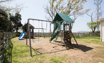 a playground with a swing , slide , and other play equipment in a grassy area near a wooden fence at Tea Trees