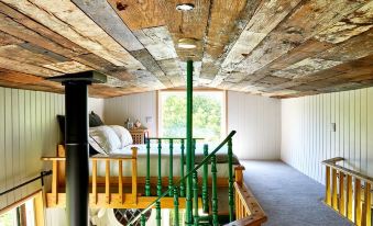 a staircase with a wooden railing leads to a loft area with a green railing at Extraordinary Huts Ltd