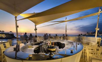 a group of people enjoying drinks at a rooftop bar , with the sun setting in the background at Kempinski Summerland Hotel & Resort Beirut